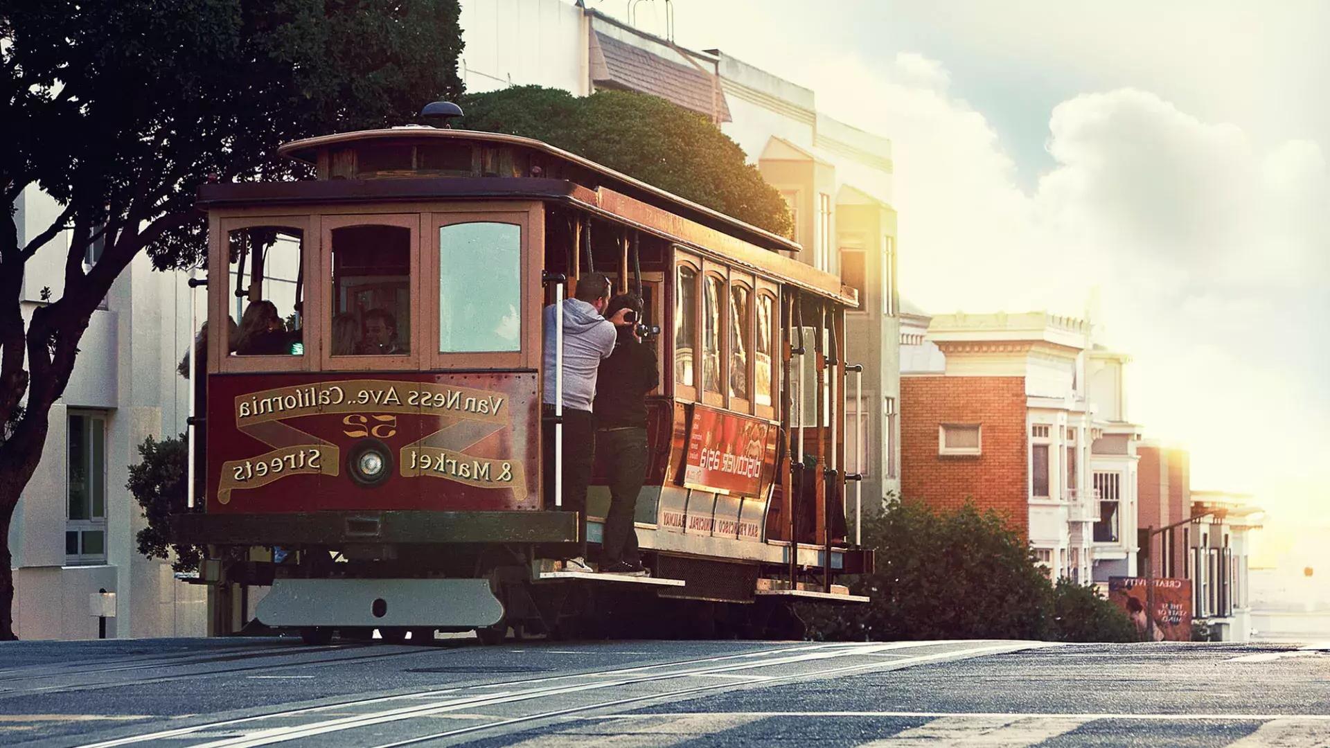 Um teleférico contorna uma colina em São Francisco com passageiros olh和o pela janela.